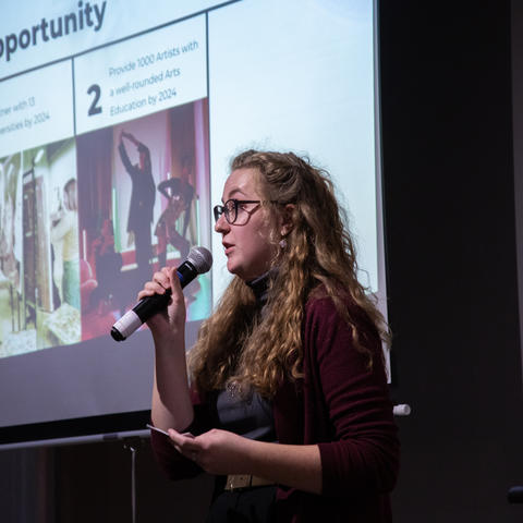 White female holding a microphone giving a presentation