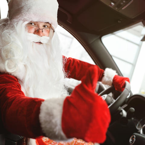 Santa Claus sitting behind the wheel of a car shows a thumbs up
