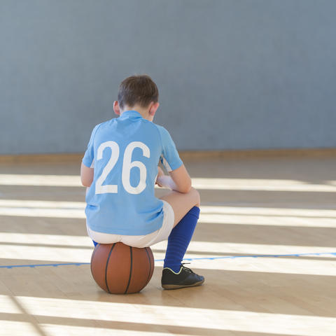young athlete sitting on a basketball