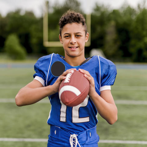 image of male-presenting adolescent in blue football jersey holding football
