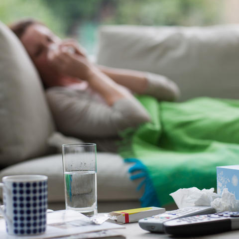 Sick woman laying on sofa blowing nose 