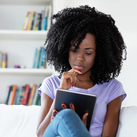photo of African American woman sitting on couch reading newspaper online