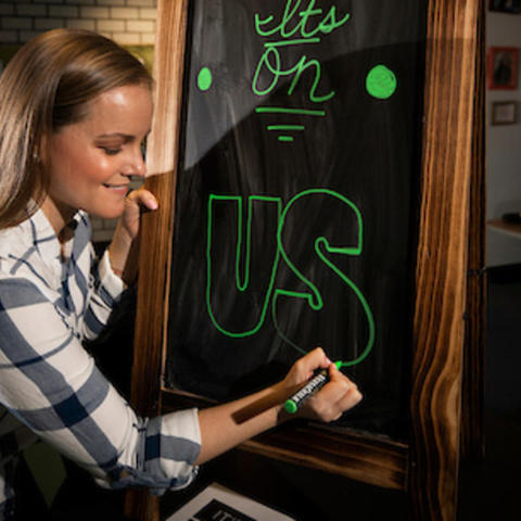 Photo of Lenzi Dodgen Writing “It’s on Us” on Chalkboard. 
