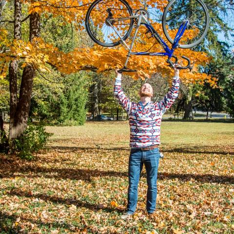 photo of Nate Williams holding bike over head with fall leaves - by Sally Horowitz Photography