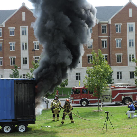photo of burn demonstration near residence halls with student watching