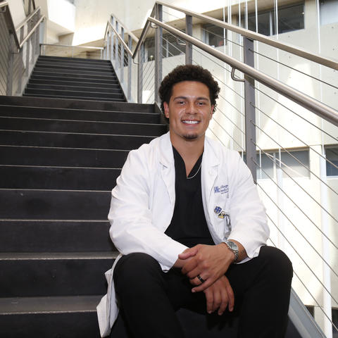 Dillon Powell in a white coat sitting on stairs