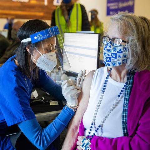 A lady wearing a UK mask and necklace receives a covid shot from a Health Sciences student