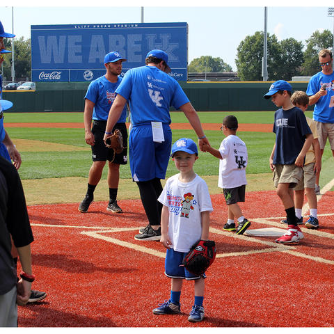 Jaxon Russell, wearing a white t-shirt and blue UK baseball hat, stands with his back facing the baseball field. 