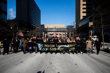 Large group marching on a snowy city street, holding a banner that reads “Martin Luther King Jr. Commemoration.”