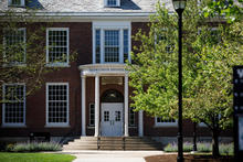 This is a front-view photo of the UK Taylor Education Building with trees and grass in sunlight in the foreground.