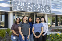 Five students stand together outside the Sanders-Brown Center on Aging, smiling for a group photo beneath the center’s sign.