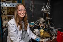 UK student Kaitlyn Brock seated next to a piece of lab equipment