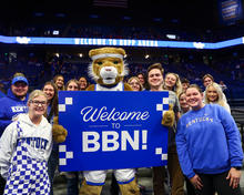 A group of students standing with the Kentucky Wildcat mascot. The mascot is holding a blue sign that says “Welcome to BBN”