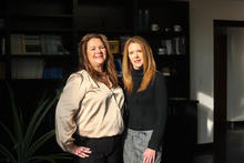 Two people standing together in a modern office with bookshelves in the background.