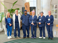 Six healthcare team members stand in a row inside a bright lobby.