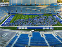 Hundreds of students gathered on Kentucky's football field pose to form a large “UK” logo inside a football stadium.