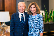 Two people standing side by side indoors, posing for a portrait in front of decorative plants and lamps.