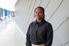 Portrait of a student standing in a bright campus hallway beside a modern gray wall.