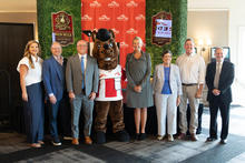 Seven people and a horse mascot stand together for a group photo in front of a red Red Mile Gaming & Racing backdrop and two “Breeders Crown Red Mile Lexington, Kentucky 2027” signs framed by green hedge panels. 
