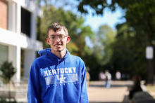 Person wearing a blue Kentucky Wildcats hoodie stands outdoors on the University of Kentucky campus.