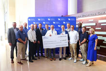 Multiple people pose with a $1.35 million Coaches for the Kids Foundation check presented to Golisano Children’s at UK in front of a blue Golisano Children’s backdrop.
