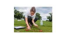 Person using a square sampling frame to examine grass in an outdoor field, with a clipboard and water container nearby.