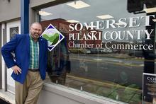 A person stands outside the Somerset-Pulaski County Chamber of Commerce office, next to a window displaying the chamber’s logo and name.
