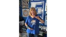 Person wears a blue T-shirt holds while standing in front of University of Kentucky-themed decorations.