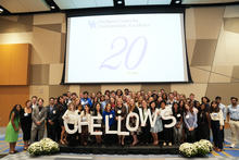 Group photo of UK fellows standing on a stage beneath a screen marking the program’s 20th anniversary.