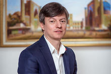 Professional head-and-shoulders portrait of a person wearing a navy blue blazer and white collared shirt.