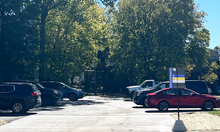 Cars parked in a tree-lined lot, with a University of Kentucky parking sign near the entrance.