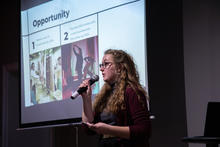 White female holding a microphone giving a presentation