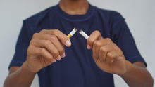 A person in a navy blue t-shirt snapping a cigarette in half with both hands.
