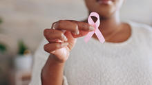 Close-up of a person holding a pink ribbon in front of a white shirt.
