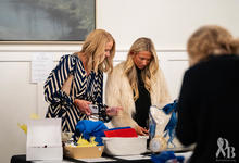 Two people look over blue, white and yellow items displayed on a table during an indoor event.