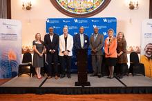 Seven people stand on a stage in front of UK HealthCare Gill Heart & Vascular Institute signage at an event.