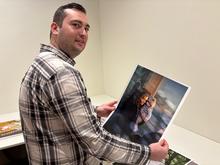 white male wearing a plaid shirt, holding a photo print, standing in a gallery with white walls