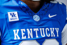 Close-up of a blue football jersey with "KENTUCKY" across the chest, featuring SEC, Nike and UK Invests patches.