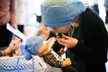 Child wearing surgical cap and examining doll 