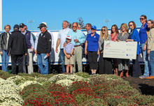 A group poses outdoors behind flower beds while several people hold an oversized $5,000 check from Red Mile for the UK MGCAE Ag Equine Programs’ Lexington Trot Breeders Association Student Scholarship.