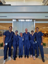 Six people in medical scrubs standing together indoors, smiling at the camera.