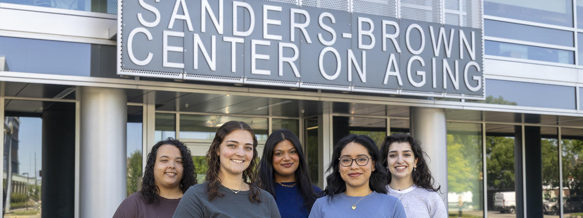 Five students stand together outside the Sanders-Brown Center on Aging, smiling for a group photo beneath the center’s sign.