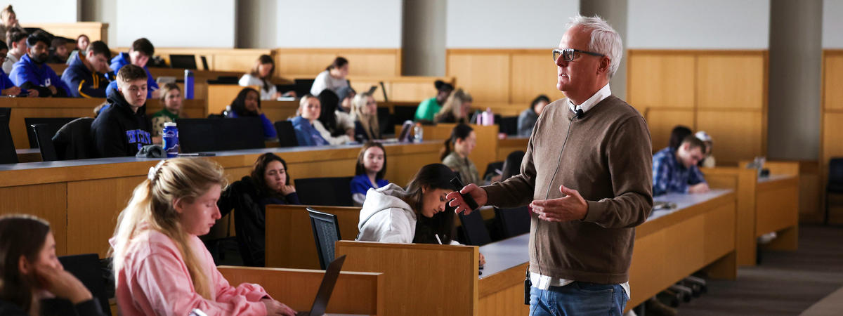 An instructor speaks to students seated in a large lecture hall.