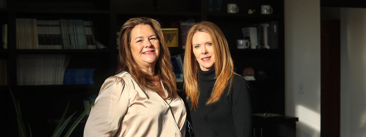 Two people standing together in a modern office with bookshelves in the background.