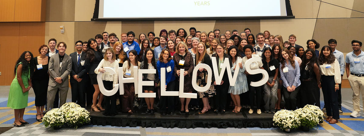 Group photo of UK fellows standing on a stage beneath a screen marking the program’s 20th anniversary.