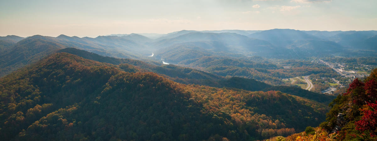 A panoramic view of forested Appalachian mountains covered in fall foliage, with a valley and community visible in the distance.