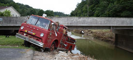 image of fire truck swept away by flood waters and stuck under a bridge