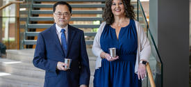 Two people stand on an indoor staircase landing, each holding a mug, with a modern stairway and large windows behind them. Provide your feedback on BizChat