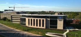 Aerial view of a modern University of Kentucky campus building beside a roadway, with surrounding green space and construction visible in the distance. 