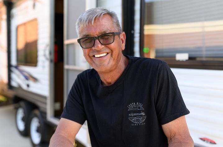 Photo of a man with silver hair wearing a black shirt in front of an RV
